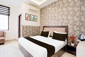 Quarto de hotel com cama, cadeira, mesa de cabeceira, cafeteira e papel de parede floral.