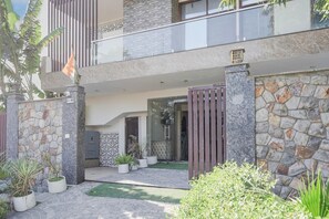 Um edifício moderno de dois andares com fachada de pedra, entrada com portão e um pequeno pátio com plantas em vasos.