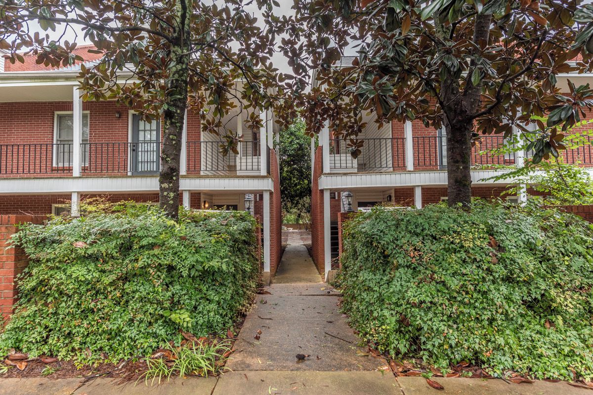 A pathway leading to a residential building with a brick facade, multiple windows, and a central entrance.