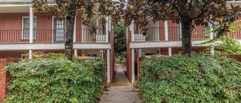 A pathway leading to a residential building with a brick facade, multiple windows, and a central entrance.