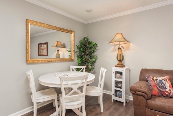 A dining area with a round table, white chairs, a large mirror, and a lamp.