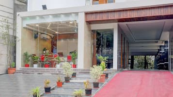 Entrada de hotel con alfombra roja, plantas en macetas y fachada de vidrio moderna.