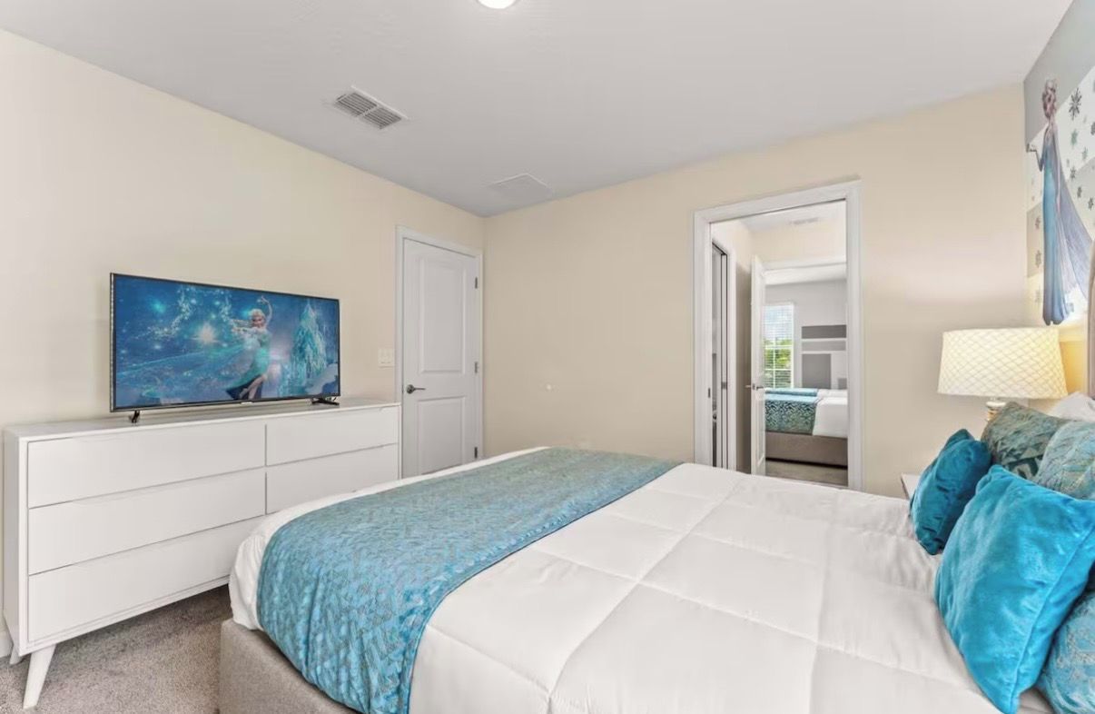 A bedroom with a bed, a dresser, a television, and a door leading to a bathroom.