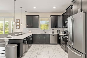 A modern kitchen with dark cabinets, stainless steel appliances, and a large window. - Family Villa Inside Resort (Four Corners)