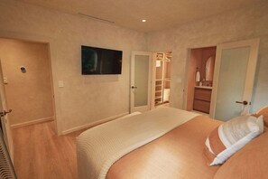 Ein Schlafzimmer mit einem großen Bett, einem an der Wand montierten Fernseher und einem begehbaren Kleiderschrank.