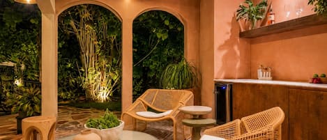 Un espace extérieur aménagé avec des meubles en osier, une table ronde et des plantes en pot.