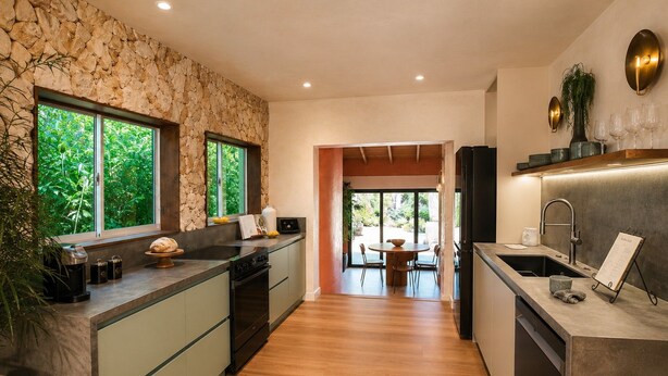 A modern kitchen with a stone wall backsplash, a central island with seating, and a view of the outdoors. - Vrbo Property (Miami)