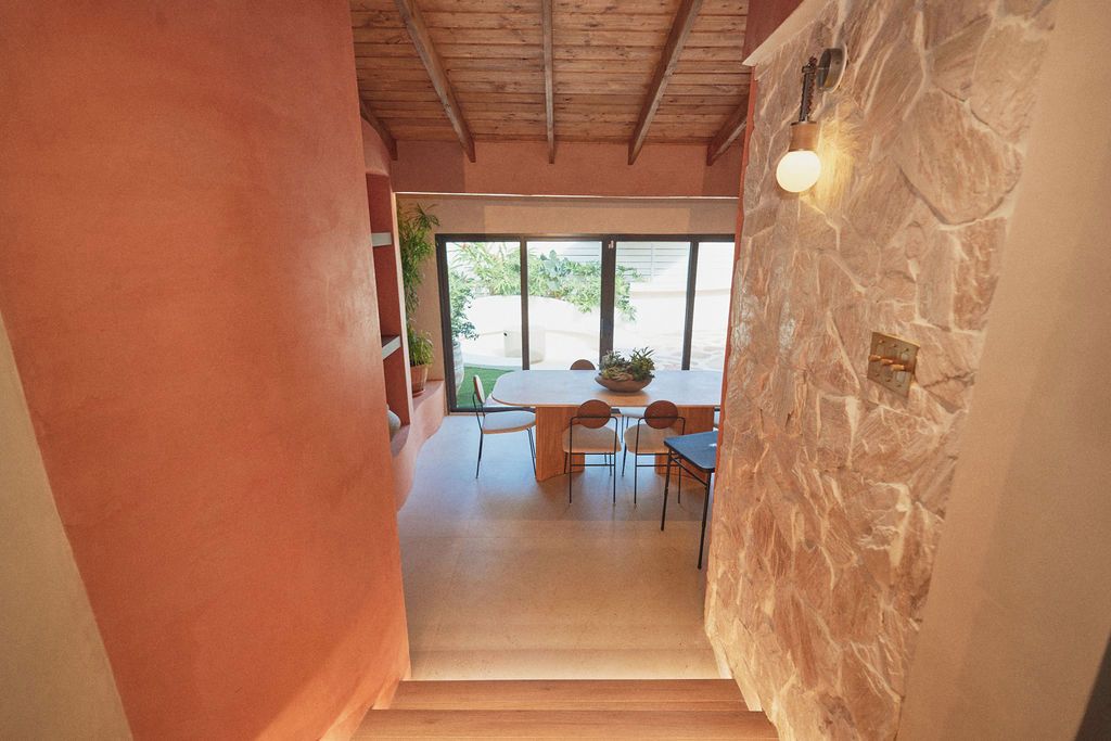 A hallway leading to a dining area with a stone wall, wooden ceiling, and a table with chairs.