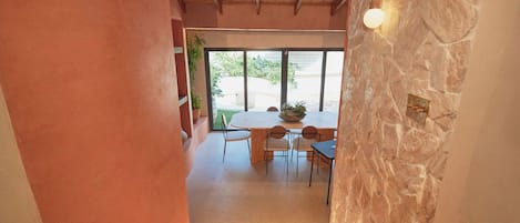 A hallway leading to a dining area with a stone wall, wooden ceiling, and a table with chairs.