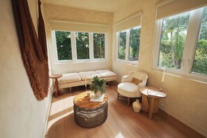 Ein Zimmer mit einer Couch, einem Sessel, einem runden Holztisch und einem Fenster mit Blick auf Grünflächen.