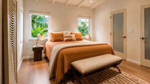 A bedroom with a large bed, a bench, two windows, a door, and a radiator. - Vrbo Property (Miami)