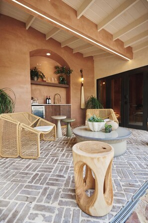 An outdoor seating area with wicker furniture, a round wooden table, and potted plants. - Casa di Arte: This luxurious 1930s Mediterranean-Nordic home blends art and architecture (Miami)