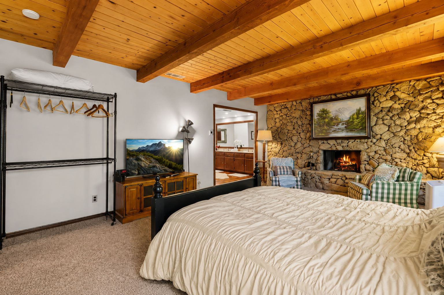 A bedroom with a bed, a television, a stone fireplace, and a stone wall.