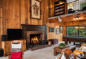 Ein gemütliches Zimmer mit Kamin, Billardtisch und einem Balkon mit Bücherregalen.