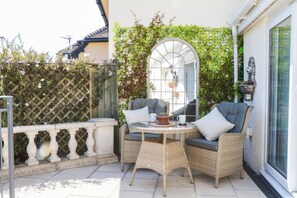 A patio with wicker furniture, a glass door, and a view of a building with a tiled roof. - Elberry Cove View (Paignton)
