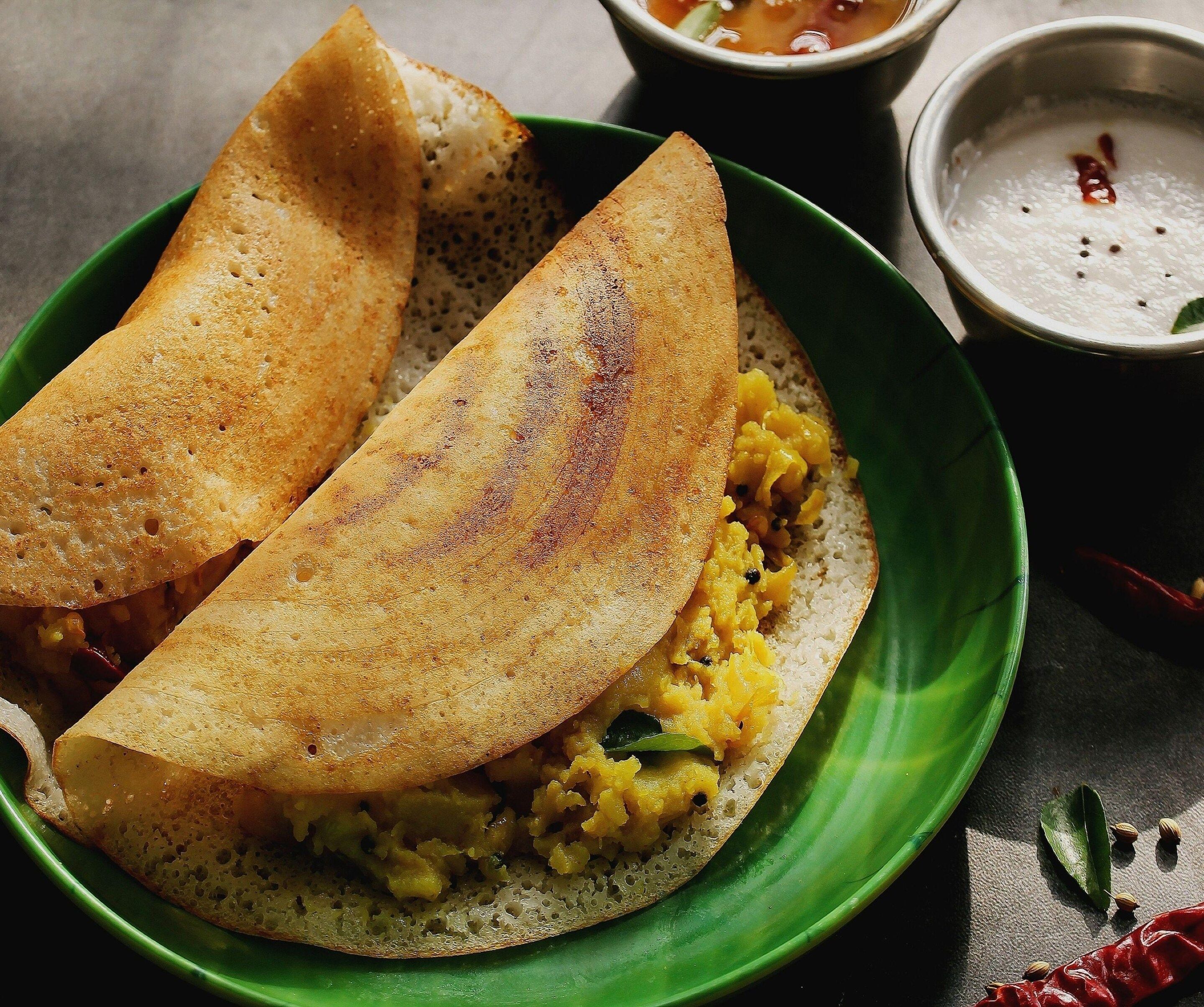 Un plato con dos medias de dosa, un tazón de sambar y un pequeño tazón de chutney de coco.