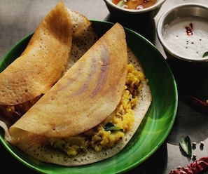 A plate with two halves of a dosa, a bowl of sambar, and a small bowl of coconut chutney.