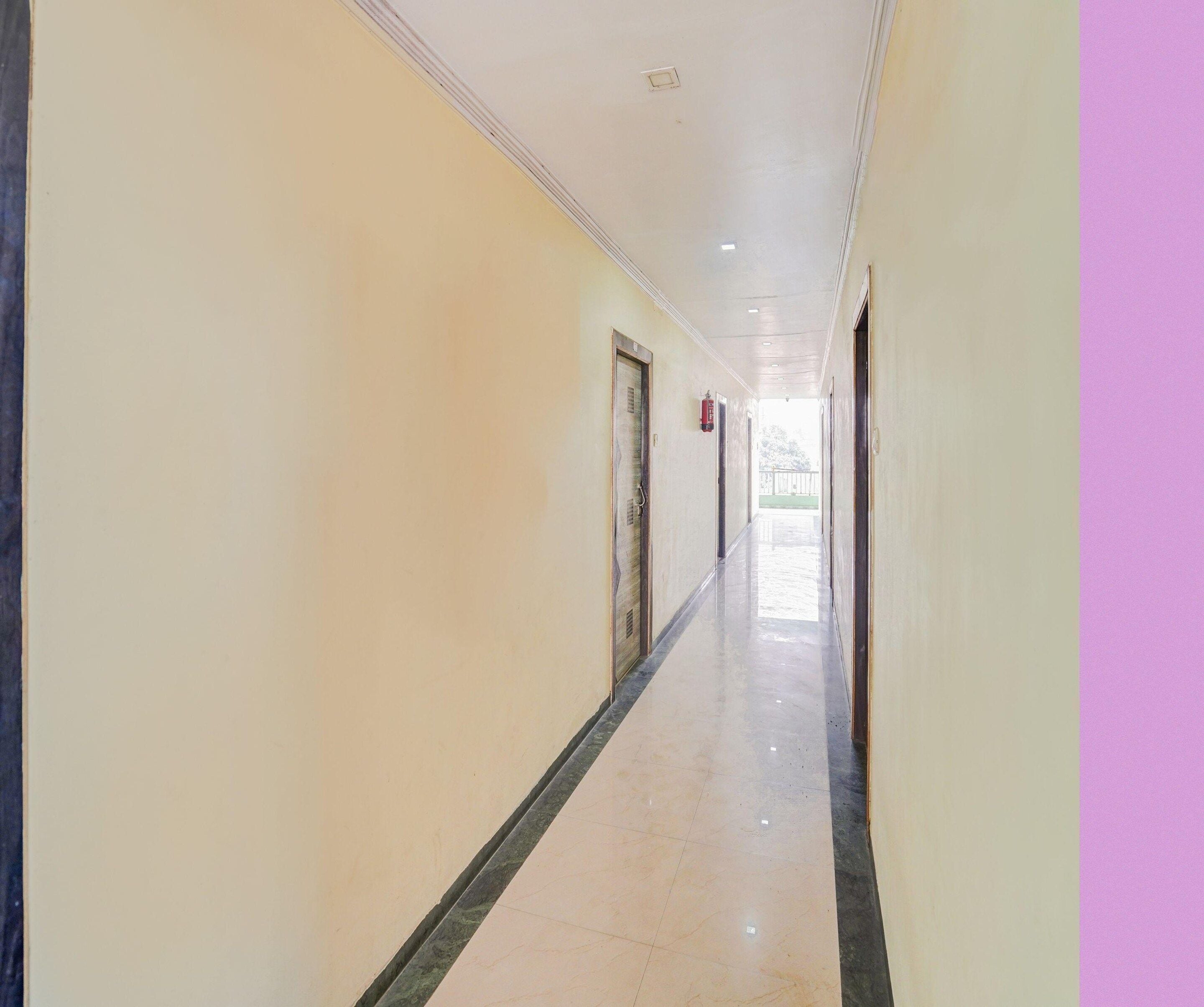 A long, narrow hallway with doors on both sides, a fire extinguisher mounted on the wall, and a tiled floor.