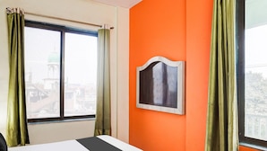 A hotel room with a bed, an orange wall, a window with curtains, and a framed picture. - Deluxe Khanka Chowk Darbhanga (Darbhanga)
