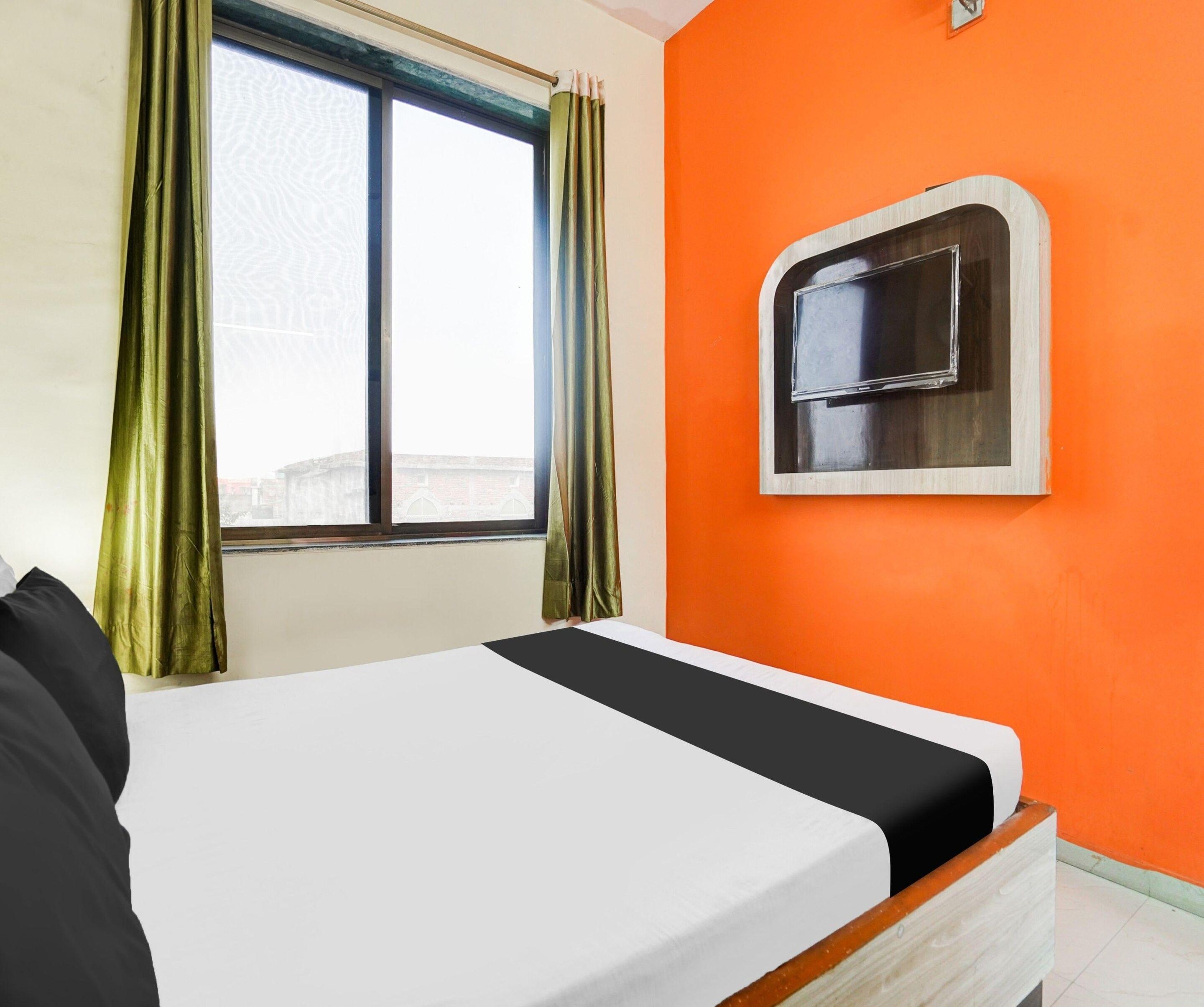 Una habitación de hotel con cama, ventana con cortinas y televisión montada en la pared.