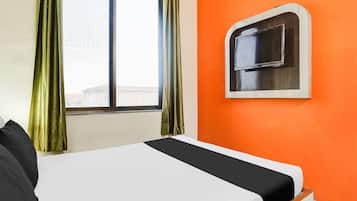 Una habitación de hotel con cama, ventana con cortinas y televisión montada en la pared.
