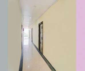 Un pasillo largo y estrecho con suelo pulido, puertas a un lado y una pared lisa al otro.