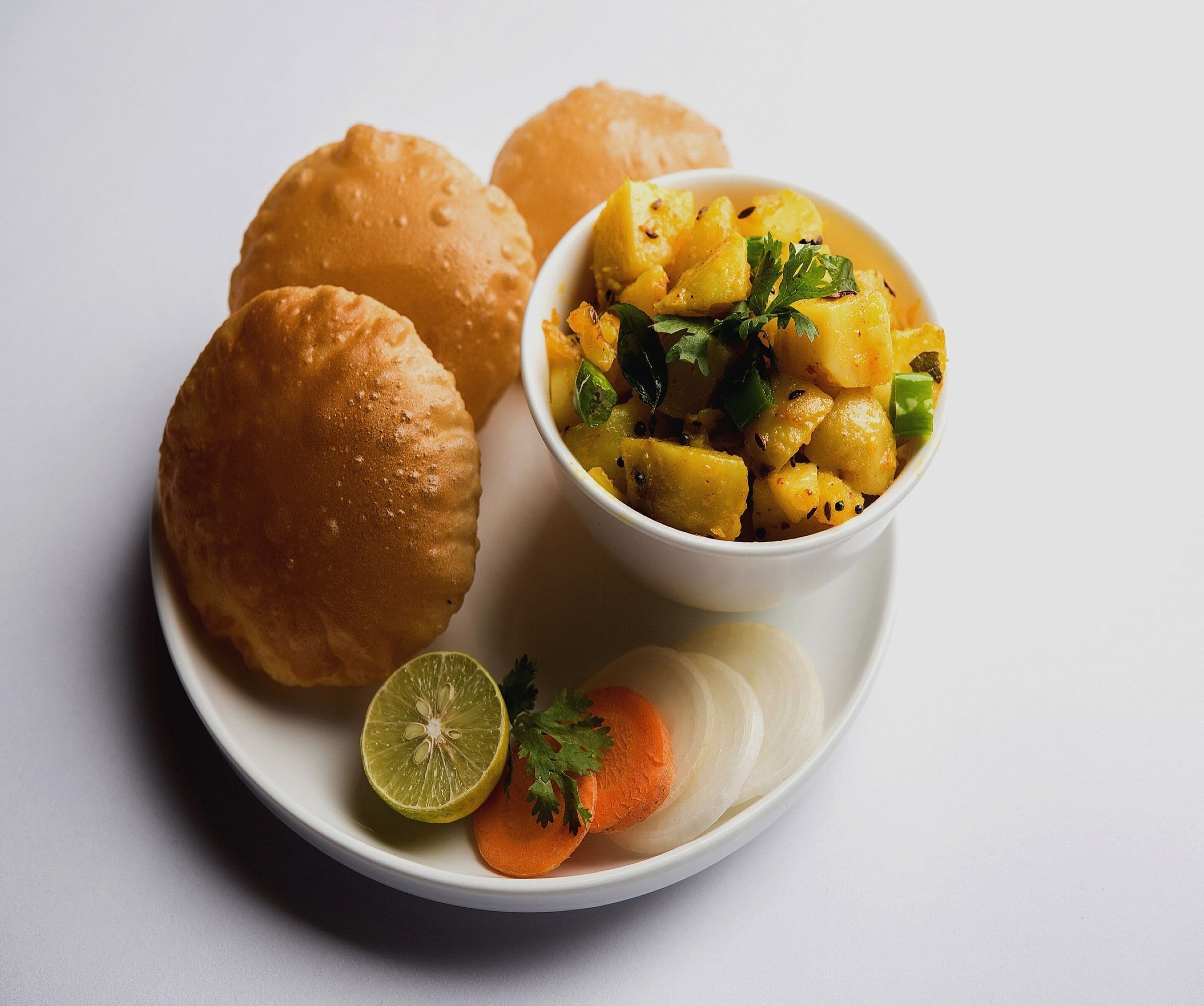 A plate with two bread rolls, a bowl of potato dish, a slice of carrot, and a lime half.