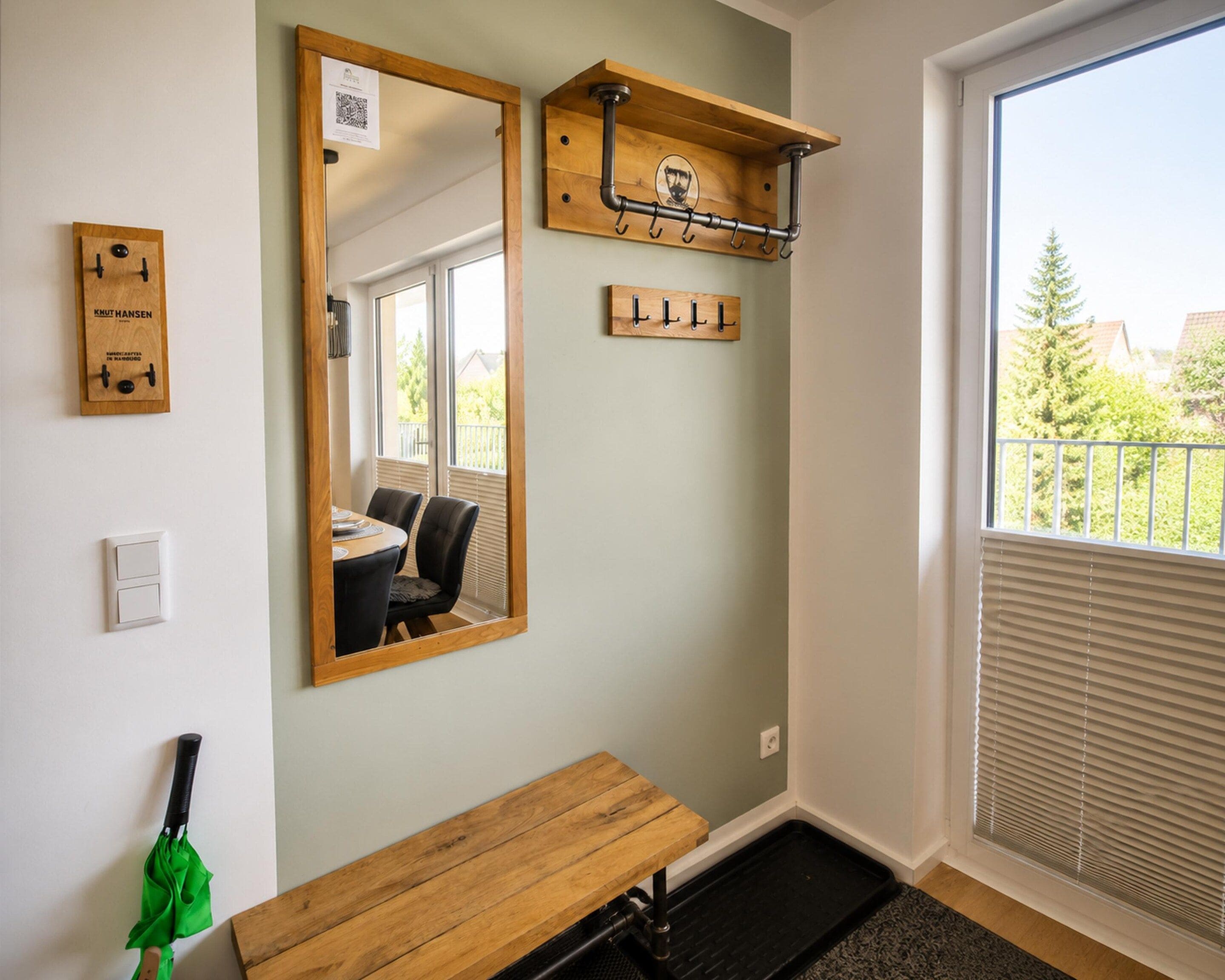 A room with a large mirror, a wooden bench, a coat rack, and a window with blinds.