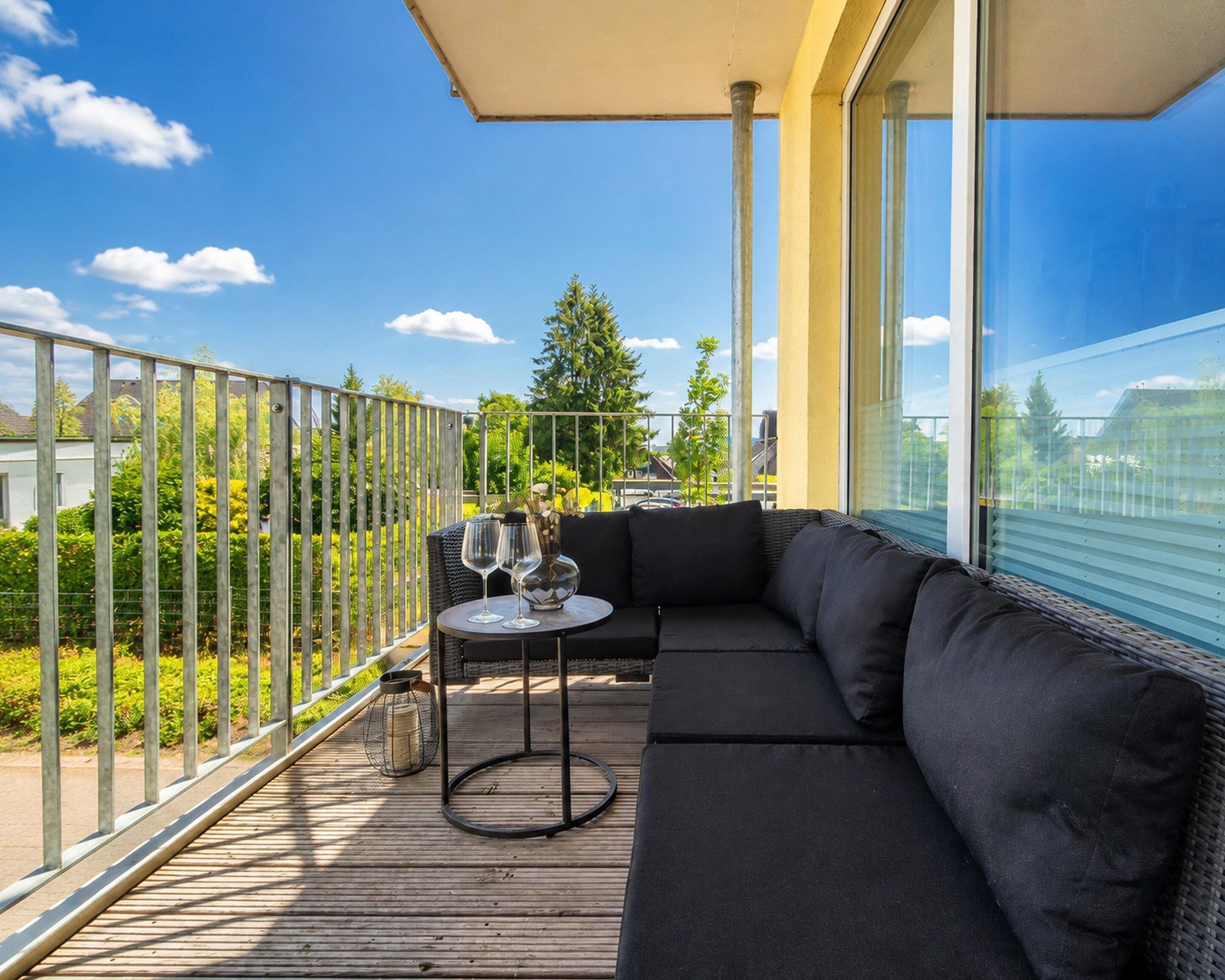 Een balkon met een bank en een klein tafeltje, een glas wijn, en uitzicht op een woonwijk.