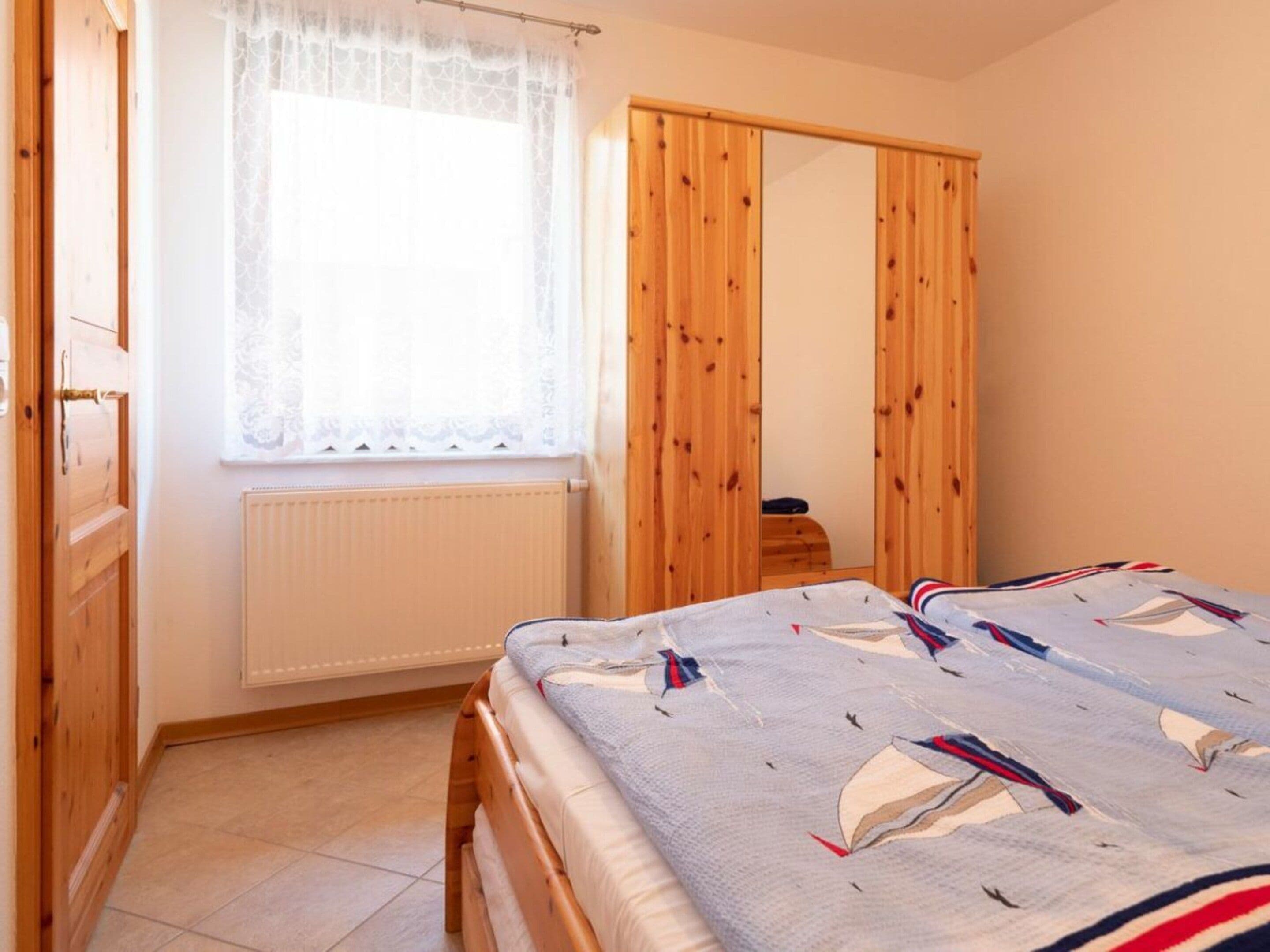 A bedroom with a bed, a window with lace curtains, a wooden wardrobe, and a radiator.