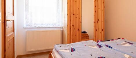 A bedroom with a bed, a window with lace curtains, a wooden wardrobe, and a radiator.