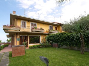 Ein zweistöckiges Haus mit Balkon, kleinem Garten und einer Palme.