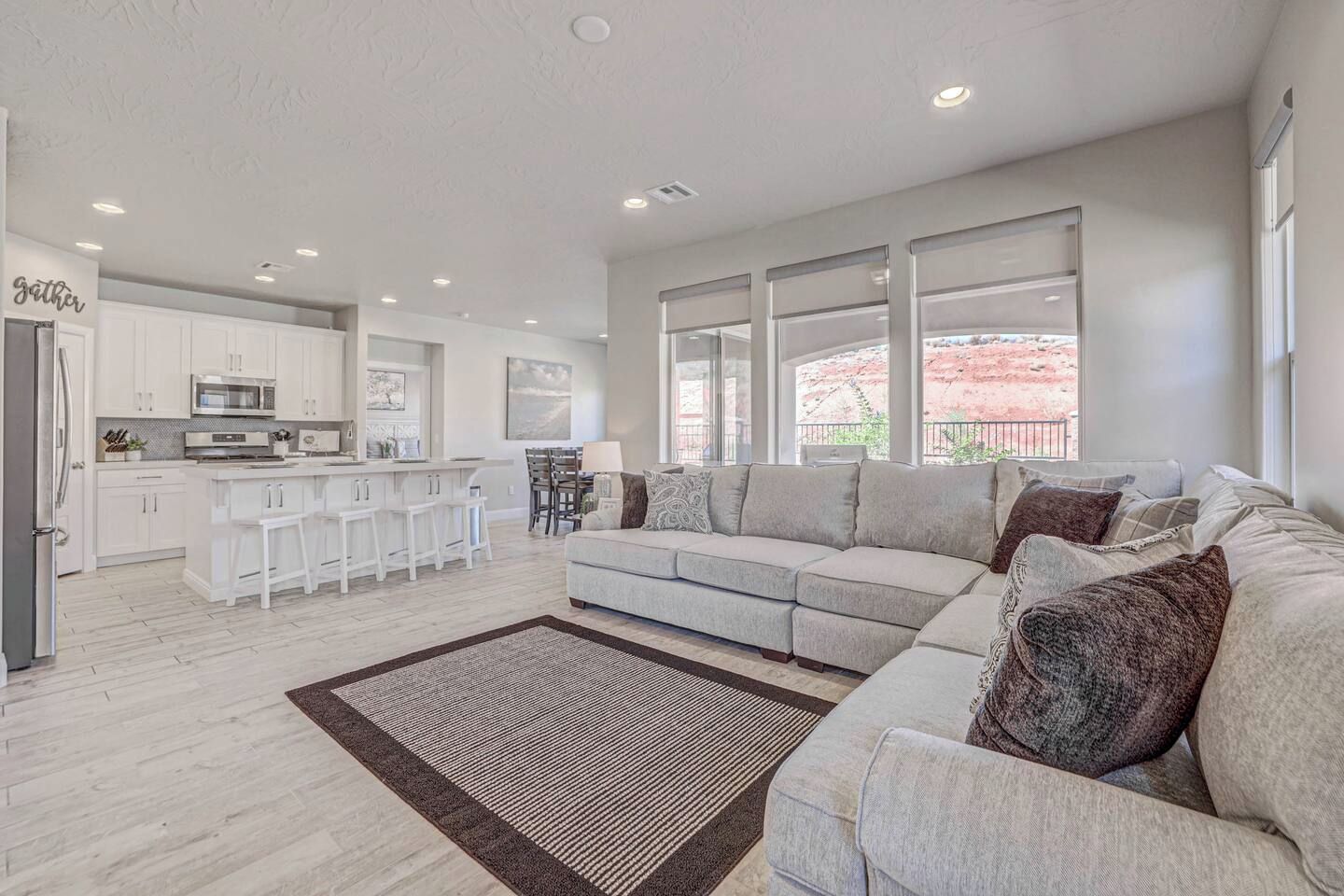 A modern living room with a grey sofa, a coffee table, and a kitchen area with white cabinets and a bar.