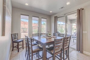 A dining area with a large table and chairs, large windows, and a view of the outdoors. - Hot Tub, Heated Pool, Ping Pong, Foosball, xBox, FastWiFi in Southern Utah (Washington)