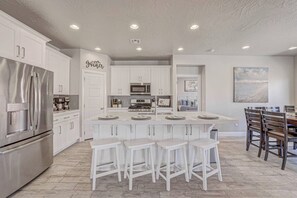 A modern kitchen with white cabinetry, a stainless steel refrigerator, and a central island with bar stools. - Hot Tub, Heated Pool, Ping Pong, Foosball, xBox, FastWiFi in Southern Utah (Washington)