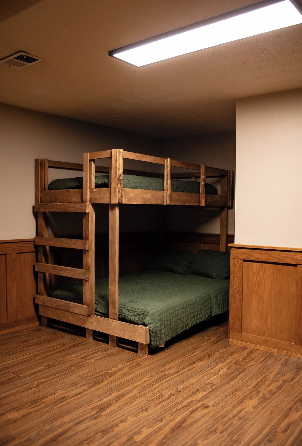 A bunk bed with a wooden frame, a green bedspread, and a ceiling light fixture.