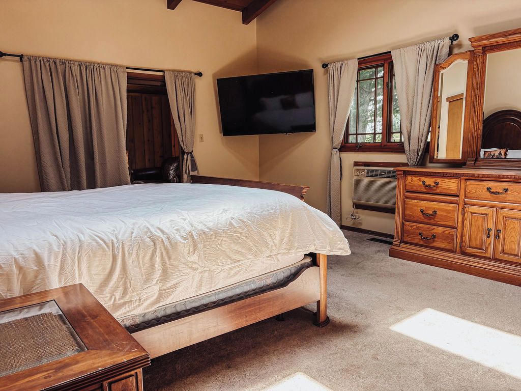 Un dormitorio con cama, cómoda de madera, televisor y ventana con cortinas.