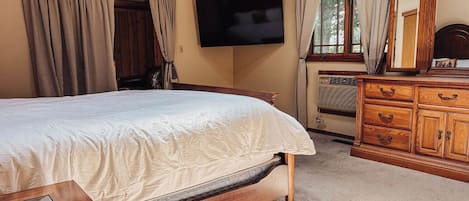 Quarto com cama, penteadeira de madeira, televisão e janela com cortinas.