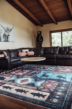 A living room with a dark leather sofa, a round coffee table, a patterned rug, a bear statue, and a framed animal print on the wall. - Rustic country getaway with private lake! - Great for large groups and families (Newark)