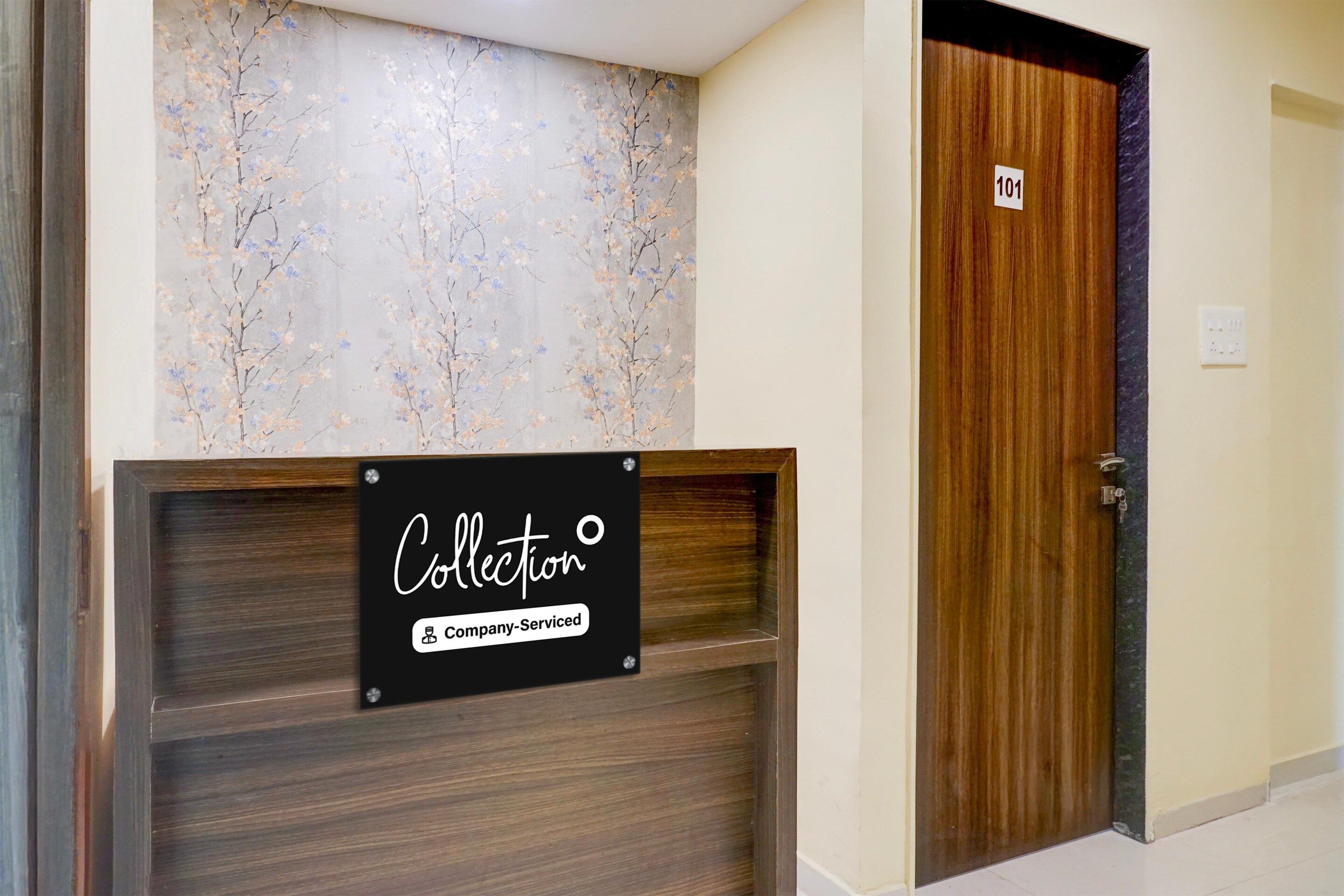 A reception desk with a sign indicating it's a company-serviced collection point, a wooden door with a number, and a wall with a floral pattern.