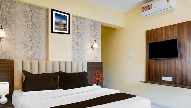 A hotel room with a bed, a wall-mounted TV, and a floral wallpaper. - Deluxe Zudio 7 Baner (Pune)