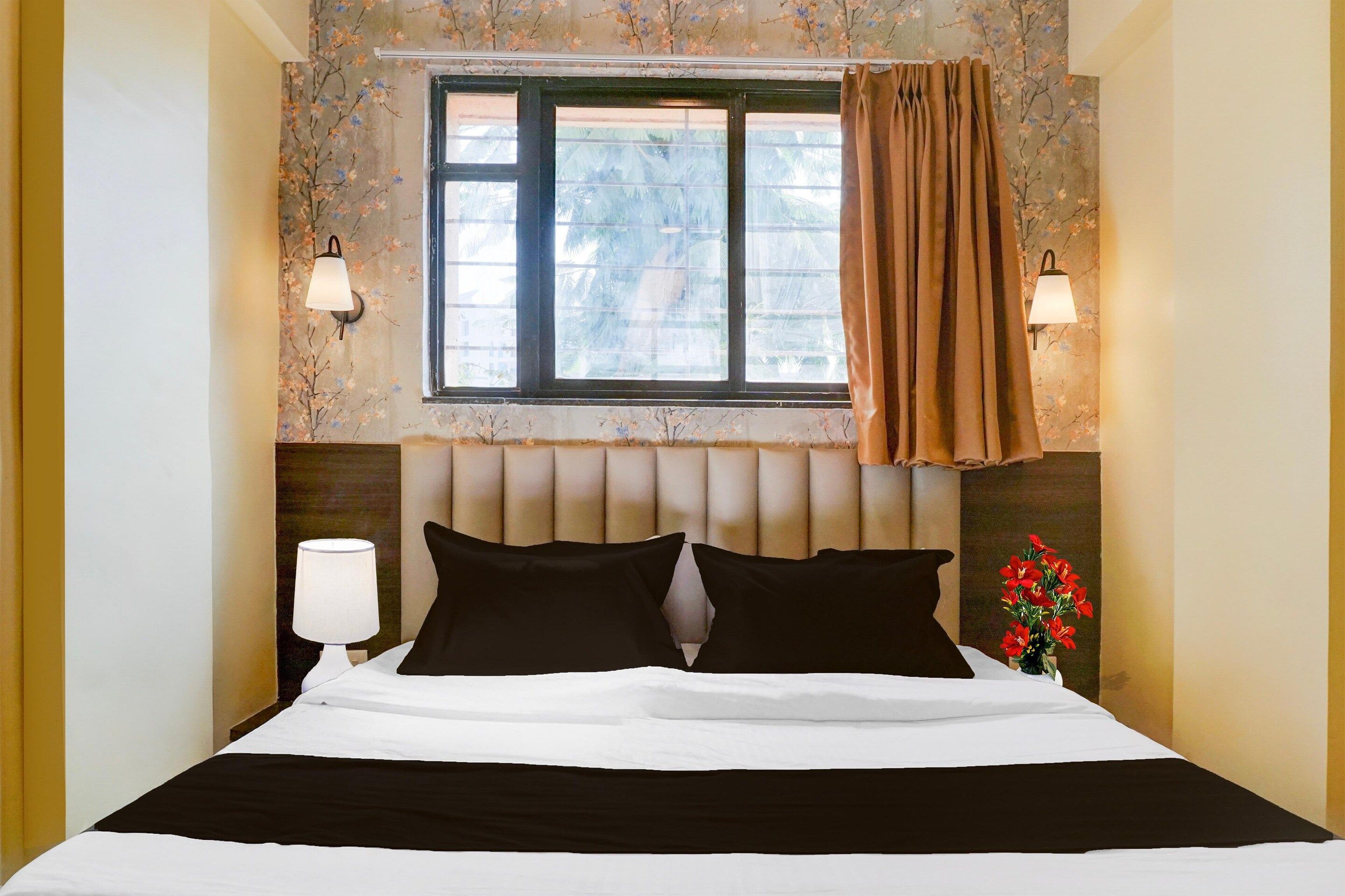 Une chambre d’hôtel avec un lit, deux lampes de chevet, une fenêtre avec des rideaux et un papier peint à motifs floraux.