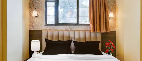 Une chambre d’hôtel avec un lit, deux lampes de chevet, une fenêtre avec des rideaux et un papier peint à motifs floraux.