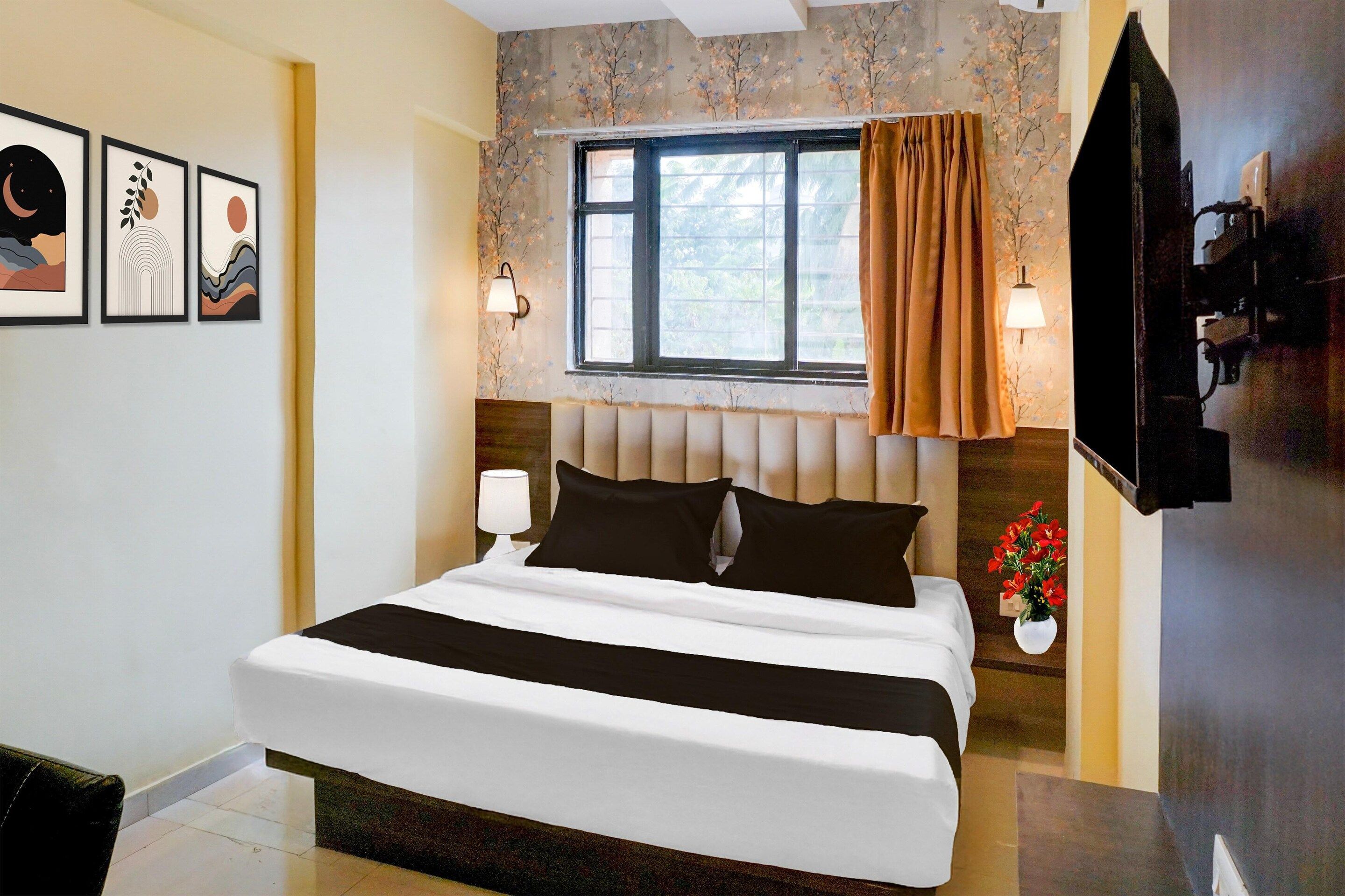 A hotel room with a bed, a window with curtains, wall-mounted lamps, and framed artwork.