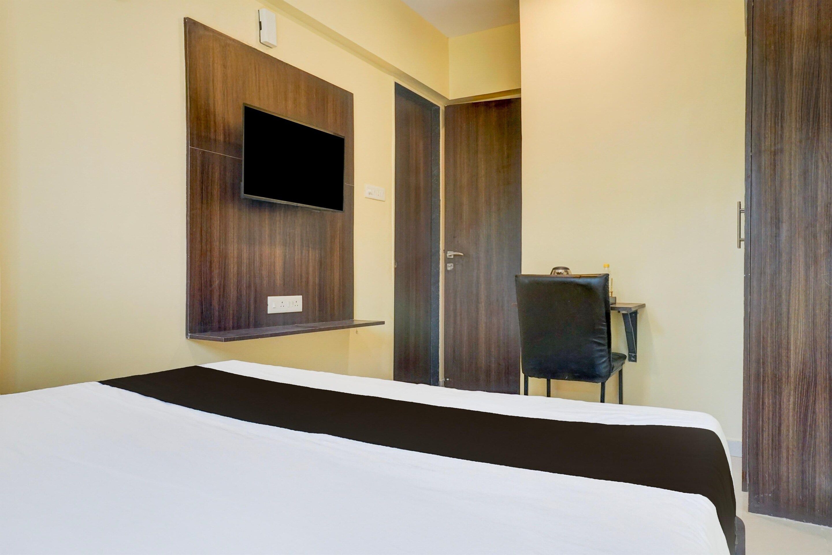 Ein Hotelzimmer mit einem Bett, einem an der Wand befestigten Fernseher, einem Schreibtisch mit Stuhl und einem Kleiderschrank.