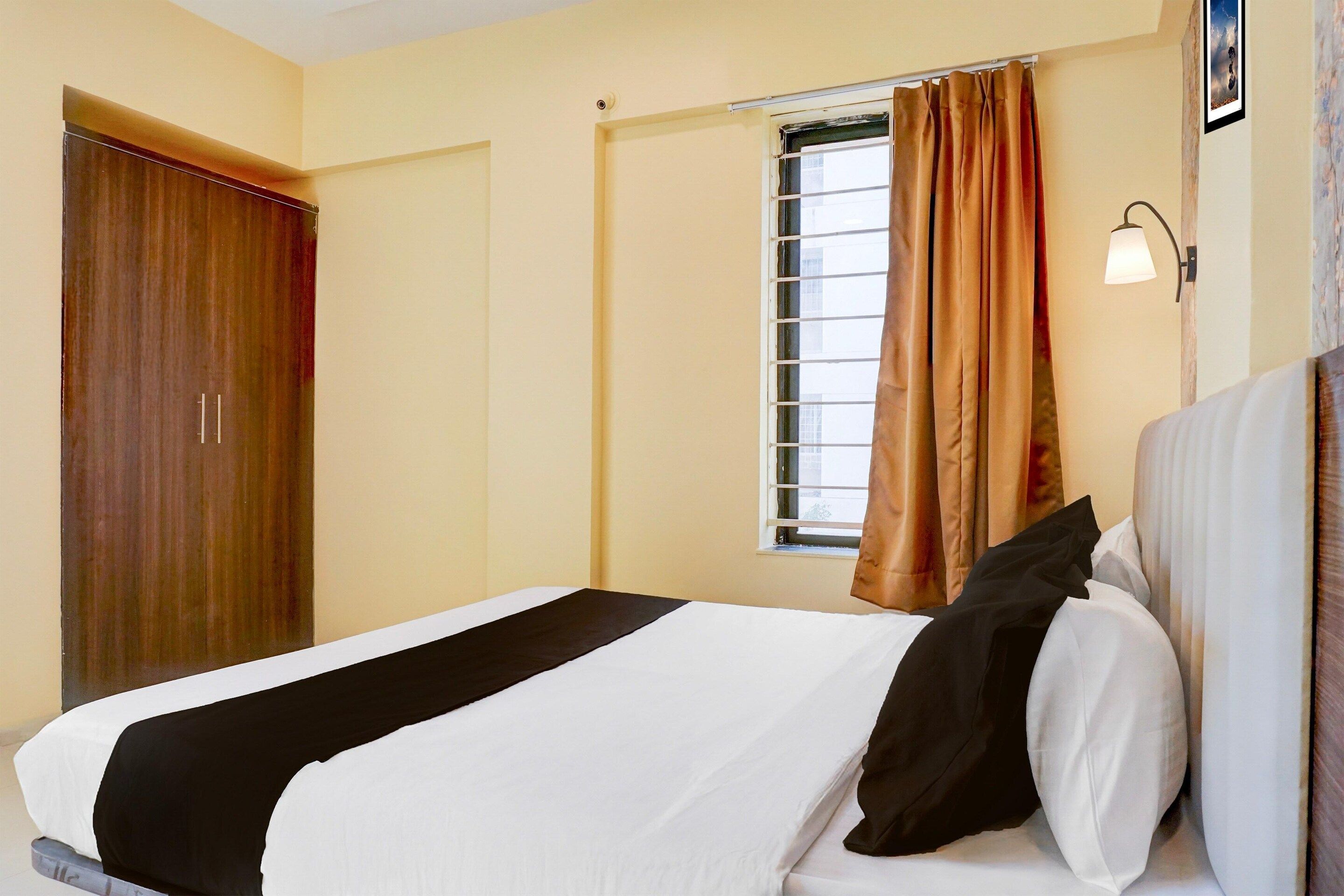 Une chambre d’hôtel avec un lit, une fenêtre avec des rideaux, une porte et un luminaire fixé au mur.