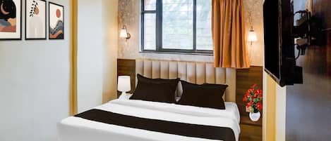 A hotel room with a bed, a window with curtains, wall-mounted lamps, and framed artwork.