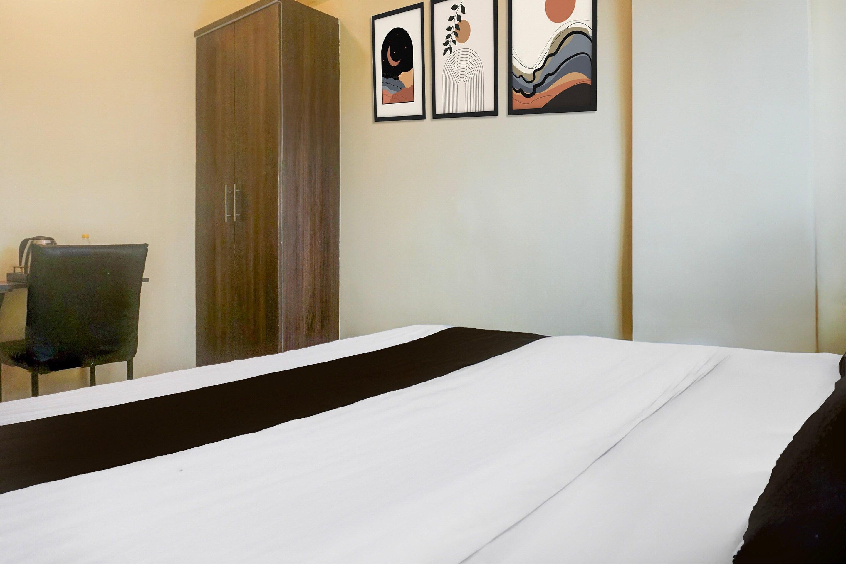 Una habitación de hotel con una cama, un armario, una silla y tres obras de arte enmarcadas en la pared.