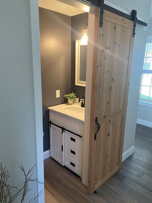 Un baño con un lavamanos blanco, un espejo y una puerta corredera de madera.