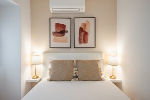 Ein Hotelzimmer mit einem Bett, zwei Wand-Klimaanlagen, zwei Nachttischlampen und zwei gerahmten abstrakten Bildern.